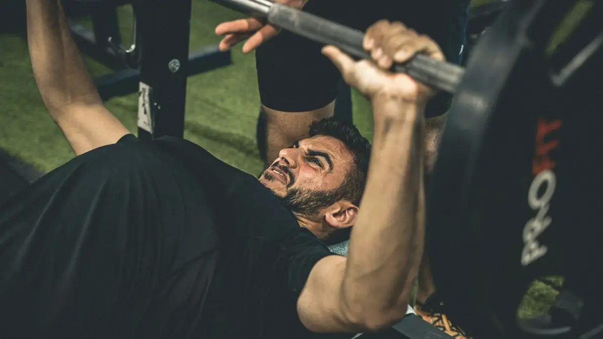 Lifter pressing a heavy barbell on the bench with a spotter &mdash; shoulder pain physical therapy for Tampa lifters at Forward Physio
