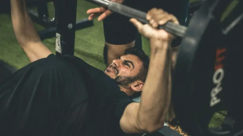 Lifter pressing a heavy barbell on the bench with a spotter — shoulder pain physical therapy guide at Forward Physio Tampa
