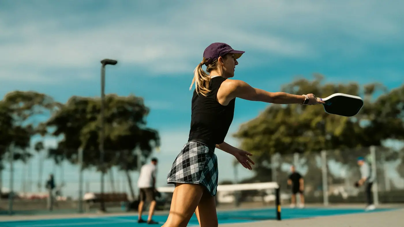 Pickleball player hitting a forehand on a sunny outdoor court — the high-volume paddle play that brings Tampa Bay players in for tennis elbow physical therapy.